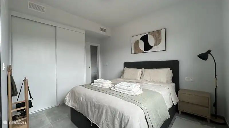 Die Schlafzimmer verfügen über einen geräumigen Kleiderschrank, in dem sogar die (leeren) Koffer gelagert werden können. An der Seite des Schranks hängt ein großer, ganzkörperlicher Spiegel. Die Stehlampe sorgt für warmes, Umgebungslicht.