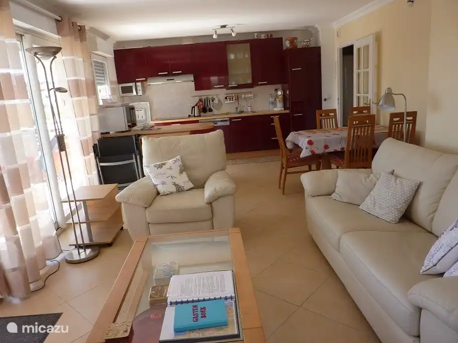 Vanuit de woonkamer kijkt u naar de volledig uitgeruste keuken met wasmachine en droger.