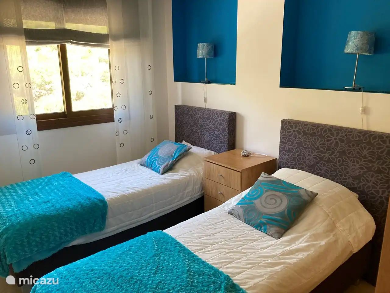 Un alegre dormitorio con dos camas individuales con somier. vista de la montaña detrás del apartamento La habitación también tiene un gran armario.