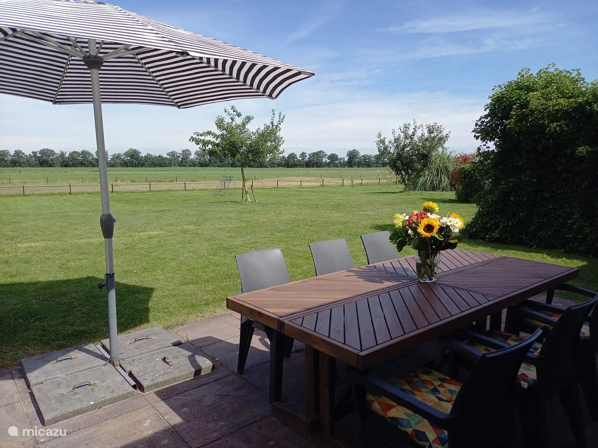 Hintere Terrasse mit großem Tisch, 6 Stühlen und großen Sonnenschirm.