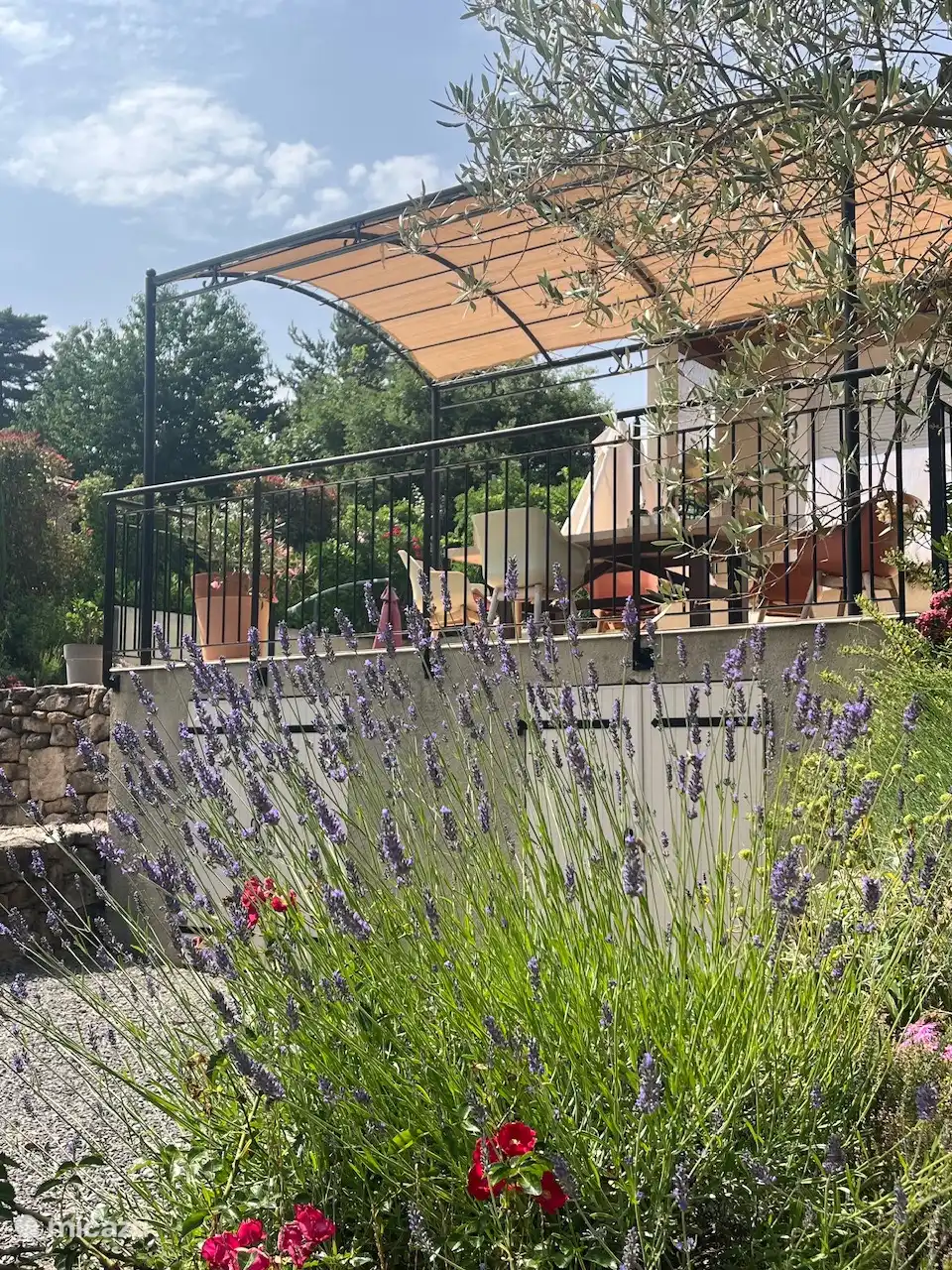 Voici une vue depuis le jardin avant vers la grande terrasse. 
Sous la terrasse se trouvent la maison de la piscine et une réserve de stockage.