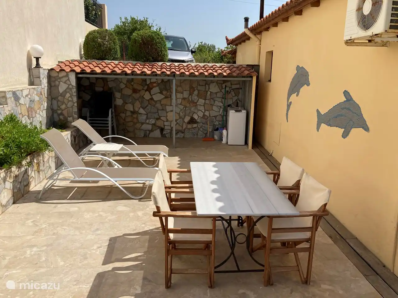 Terrasse neben dem Ferienhaus mit Marmortisch mit 4 Stühlen und Stauraum mit Waschmaschine.