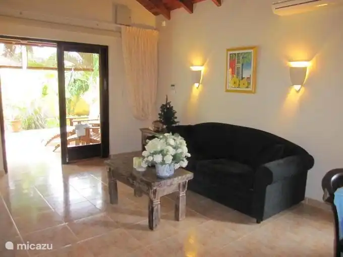 De woon/zitkamer met openslaande deuren naar het terras en zicht op de tropische tuin.