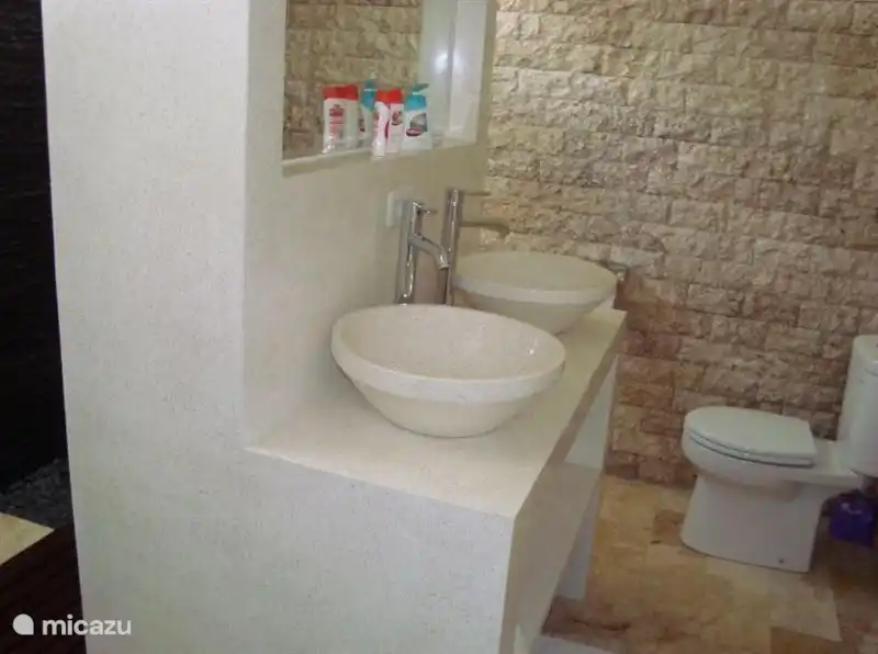 De ruime luxe badkamer met toilet is opgetrokken uit natuursteen en heeft dubbele wastafels.