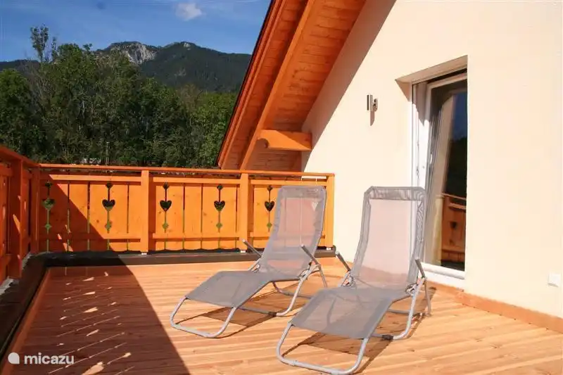 Terrasse ensoleillée et spacieuse sur le toit avec chaises longues et vue sur les pistes de ski.