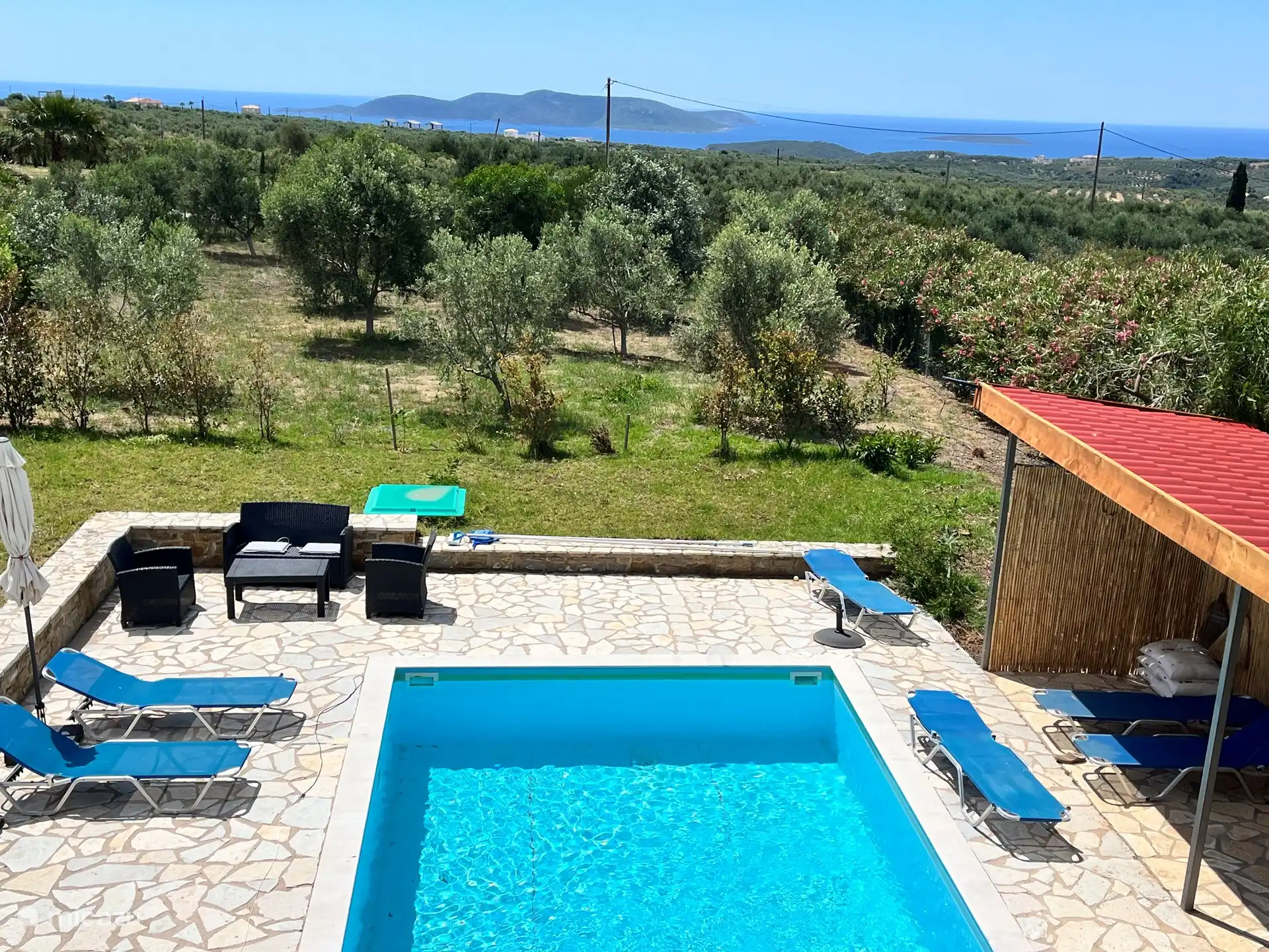 Zwembad, olijfboomgaard en tuin,  en de zee met de eilanden gezien vanuit het terras boven. 