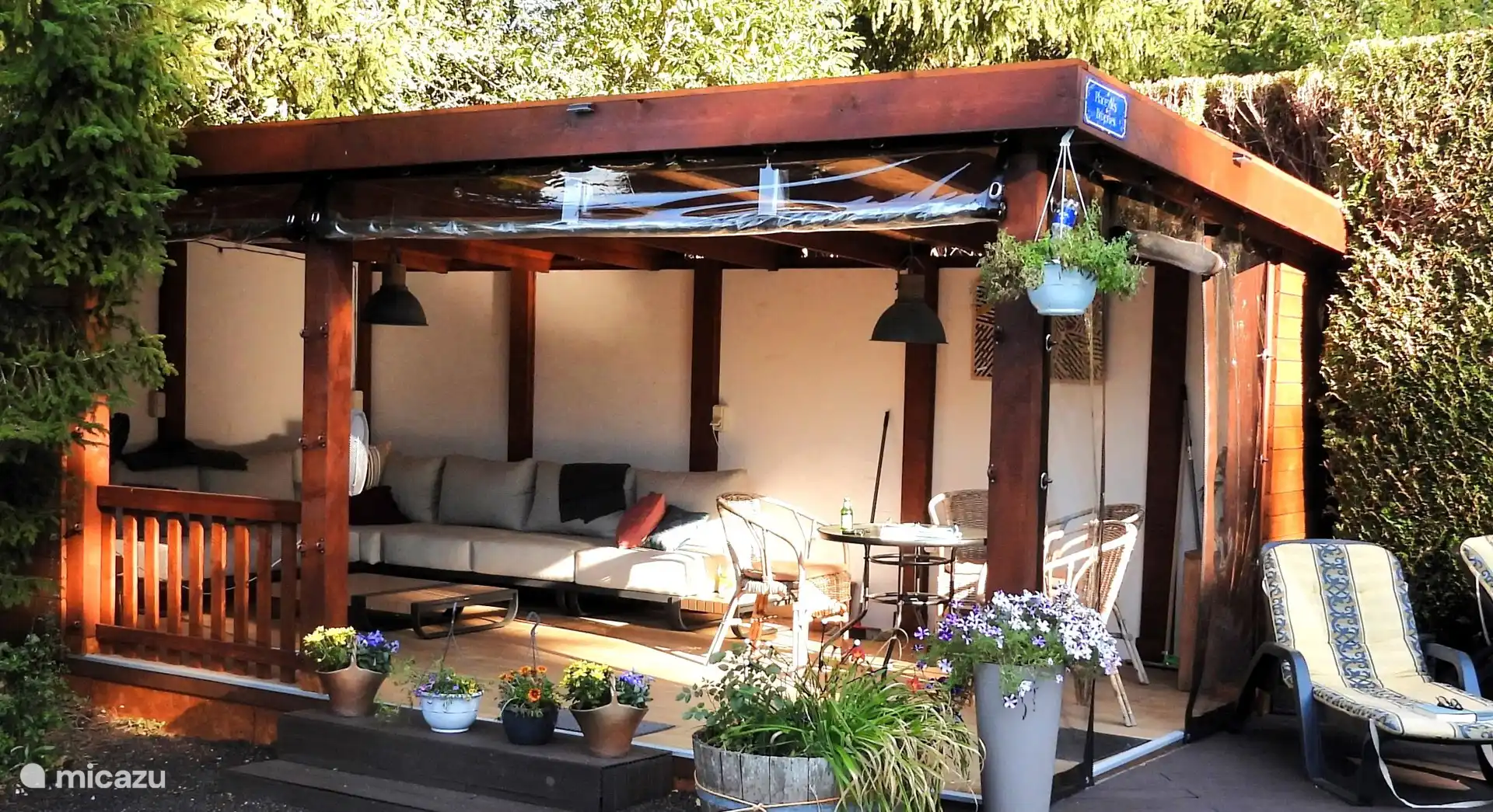 Terraza cubierta junto a la piscina, con sofá tipo lounge y asientos. Para días de lluvia, se pueden bajar las pantallas.