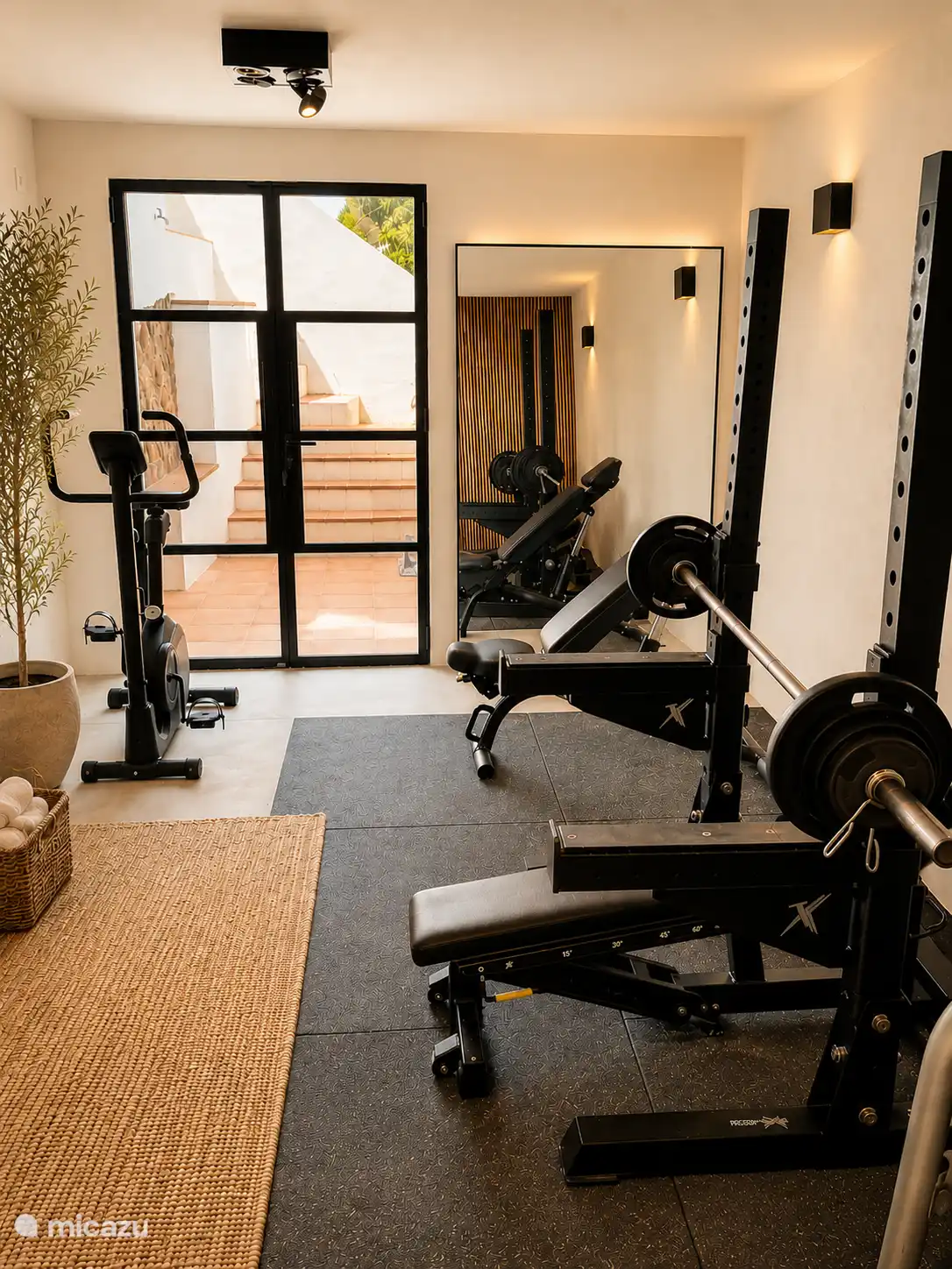 Compact gym with Technogym weights, fitness bench, multi-gym, exercise bike and yoga mats.