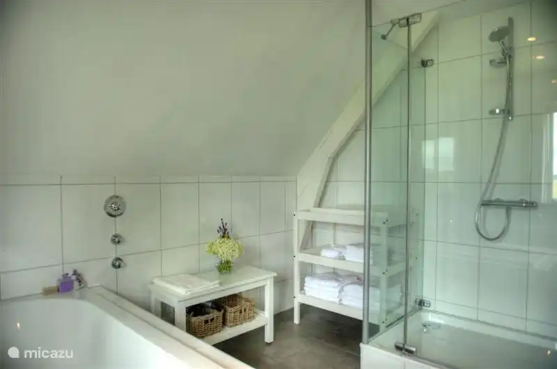 salle de bain avec baignoire au milieu de la pièce, douche spacieuse, 2 vasques, banquette, commode, sèche-cheveux.