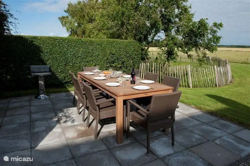 Terrasse avec grande table en teck et chaises en osier et barbecue. Derrière la terrasse, vous pouvez voir la clôture avec l'étang.
Il y a aussi un foyer pour se chauffer les soirées fraîches.
Il y a une petite table similaire dans la buanderie à rejoindre (si vous êtes à plus de 8 personnes)
