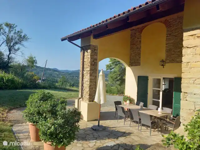 Maison Sulie | Italie, Piémont, Cartosio - maison de vacances Dans le portique (terrasse partiellement couverte) une grande table à manger pour huit personnes. L'après-midi un endroit ombragé.