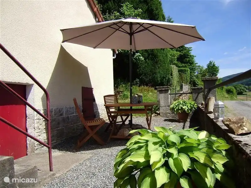 Het terras voor het huis, voorzien van parasol en tuinmeubilair.