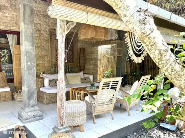 Villa Rumah Pantai No.14 huren in Indonesië, Bali, Jasri - villa De veranda met heerlijke ruime zit/loungebank met plafondfan. Je bent hier niet weg meer te slaan.. kijkend op de vijver met pergola gemaakt van bamboe met prachtige lilla hangbloemen die net op orchideeen lijken.