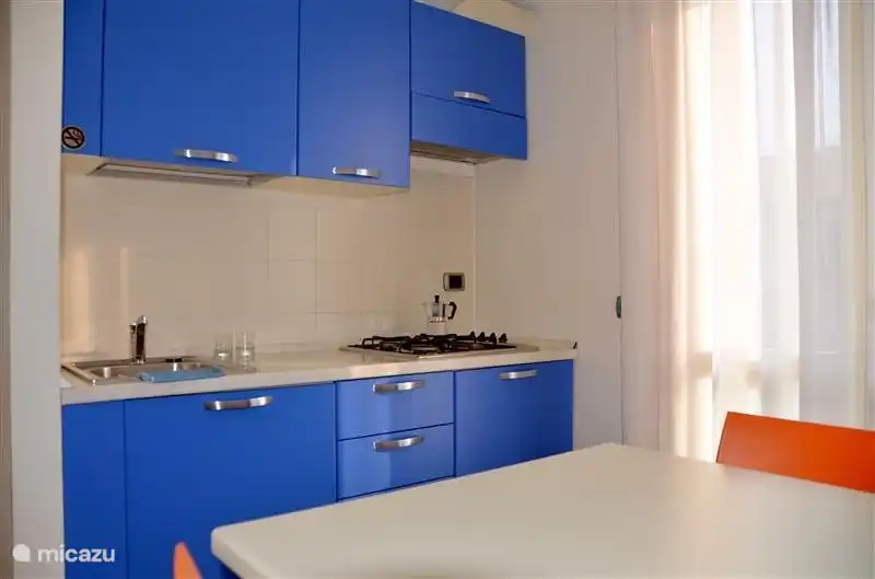 Una mirada a la cocina, con una estufa de gas de 4 quemadores, un comedor para 5 personas, refrigerador, microondas, tetera, tostadora y cafetera.