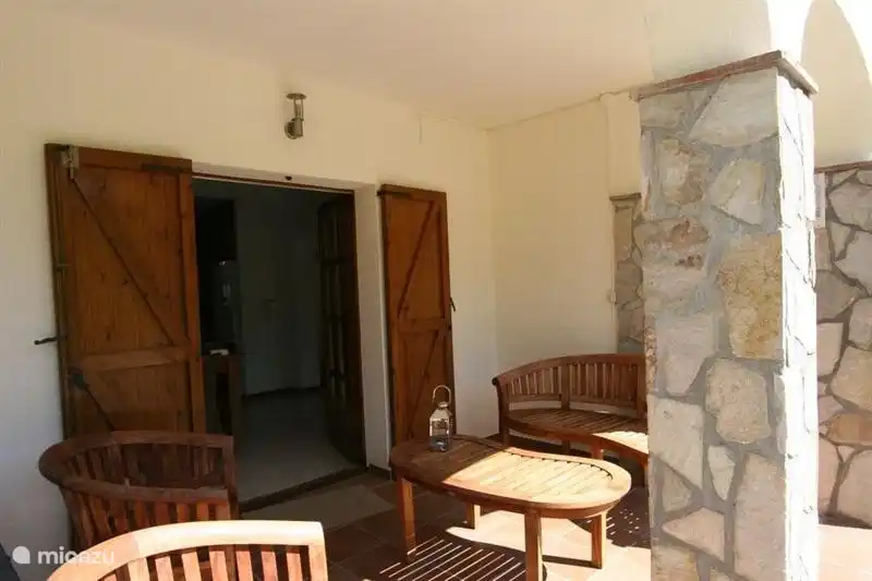 Covered patio with wooden bench, two chairs and table.