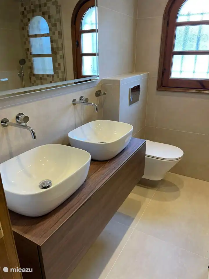 Modern bathroom in master bedroom, with sinks, toilet and walk-in shower.