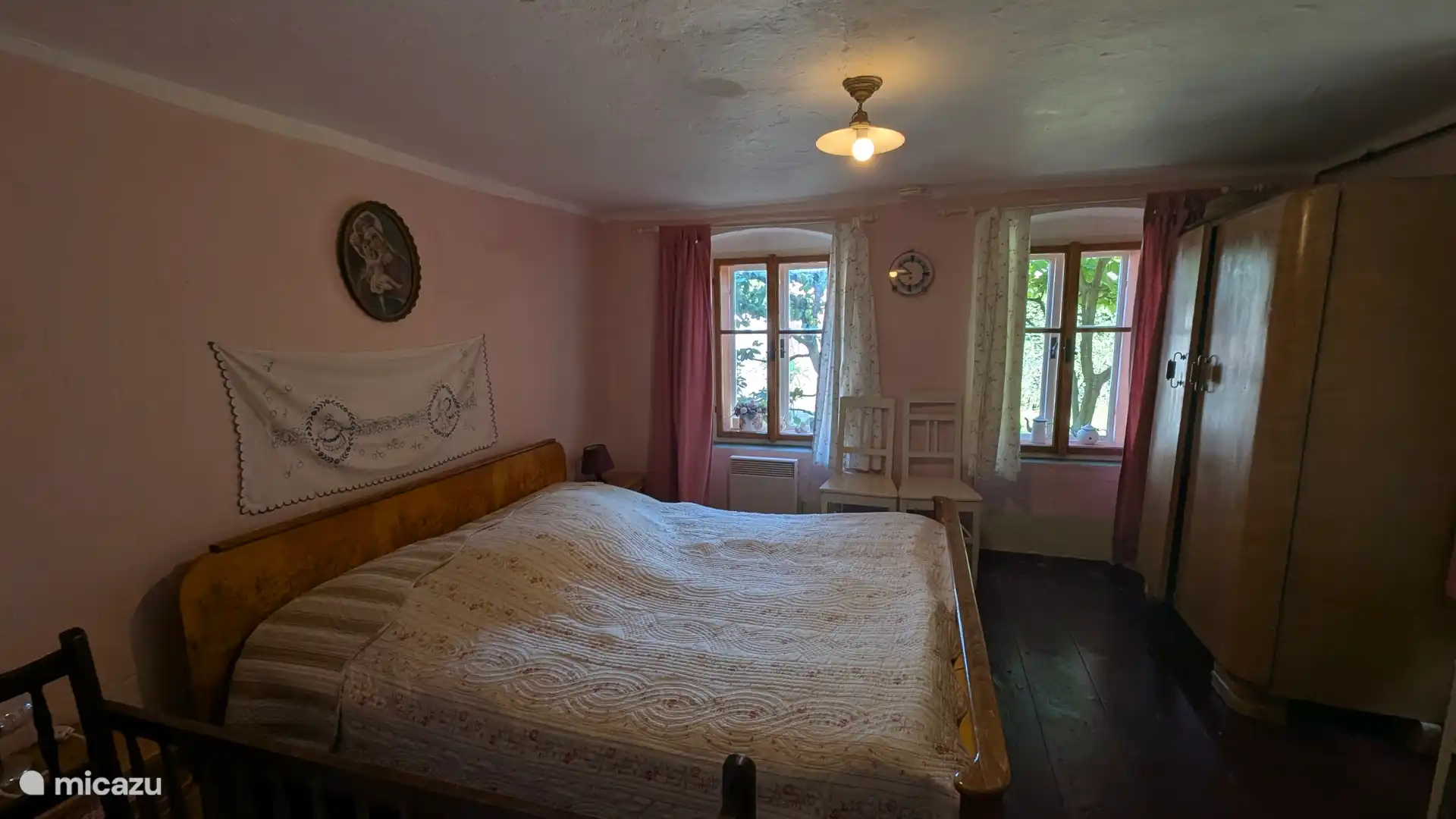 Een slaapkamer aan de voorkant van de boerderij op de begane grond in de nog bewaarde originele stijl van beging 20ste eeuw met zicht op het dorpspleintje met kerkje.