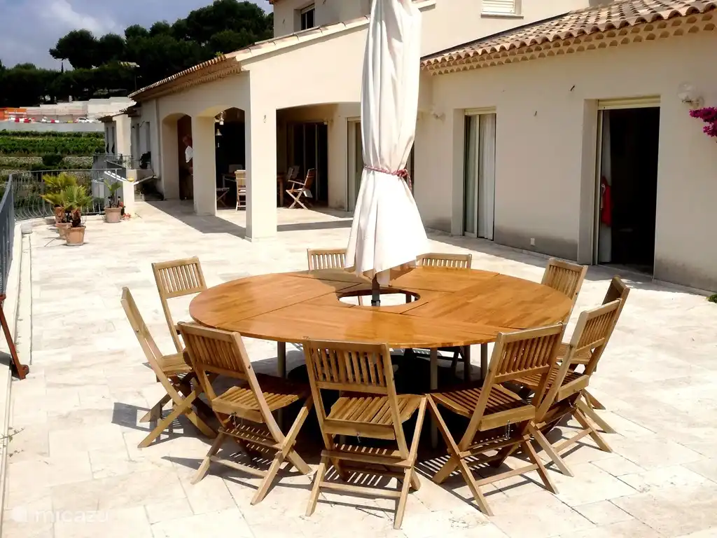Der runde Tisch auf der großen Terrasse mit dem (überdachten) Außentisch vor der Küche im Hintergrund.
