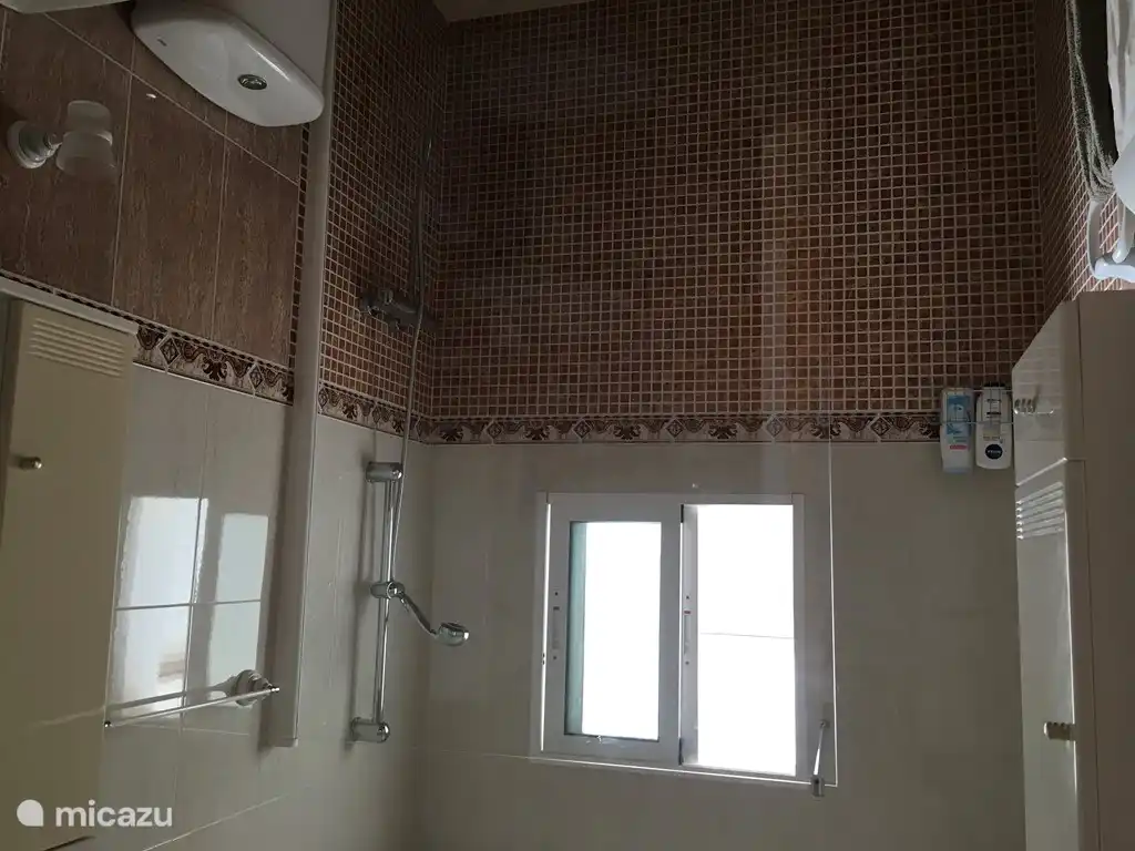 El baño con inodoro, lavabo, ducha a ras de suelo y tocador.