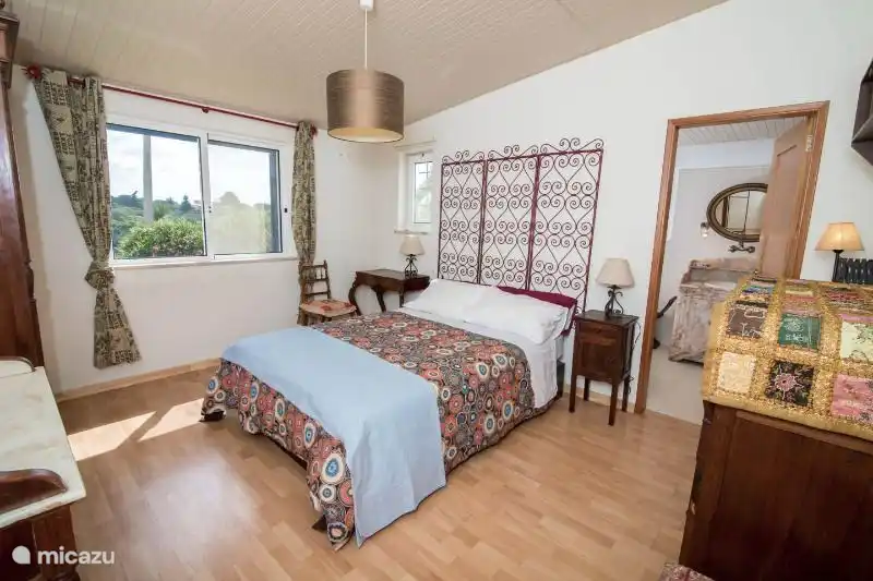 Schlafzimmer mit Doppelbett und angrenzendem Bad. Das Badezimmer hat eine Toilette, Waschbecken und Badewanne mit Dusche.