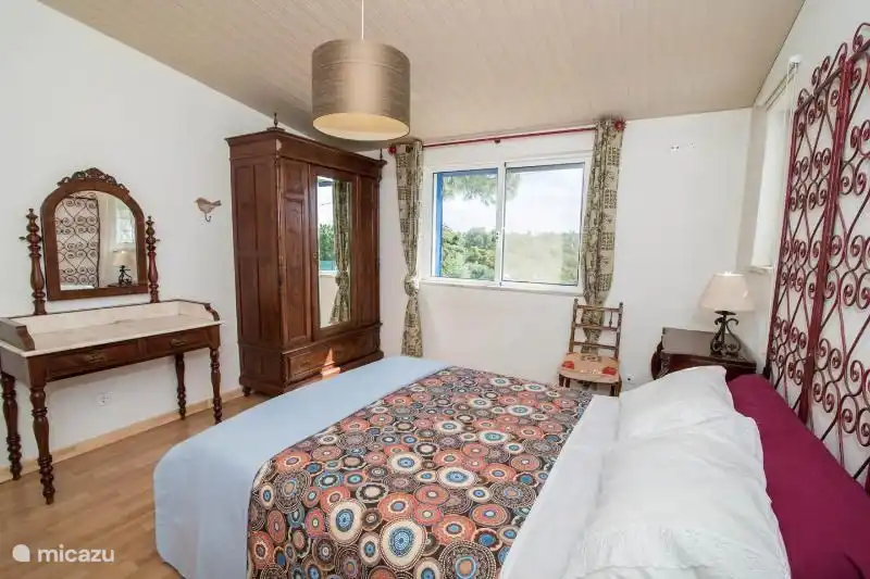 Schlafzimmer mit Doppelbett und angrenzendem Bad. Das Badezimmer hat eine Toilette, Waschbecken und Badewanne mit Dusche.