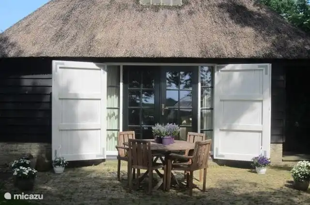 uitzicht vanuit de tuin op het vakantiehuis en terras. Tafel en stoelen zijn aanwezig