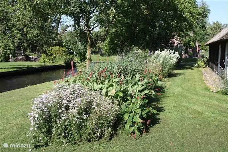 De fraai aangelegde ruime tuin met planten, groot grasveld en grenzend aan het water