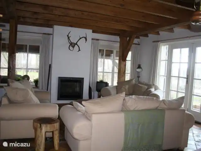 Dwarsgracht 39 en Países Bajos, Overijssel, Giethoorn - casa de campo La acogedora sala de estar con asientos alrededor de la chimenea (eléctrica). Hay un televisor y suficiente luz para leer un libro. Si prefiere sentarse afuera, las puertas del patio lo llevan a la terraza con sillas y mesa de madera con vista al jardín, al agua y al Weerribben-Wieden.