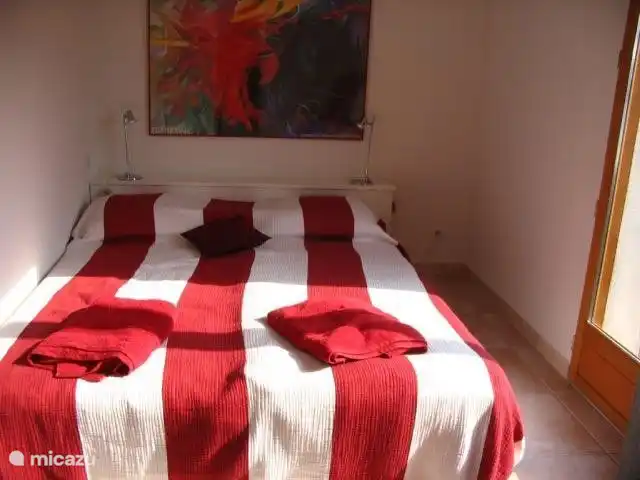 Chambre rouge au rez-de-chaussée avec lit double et portes-fenêtres donnant sur le jardin