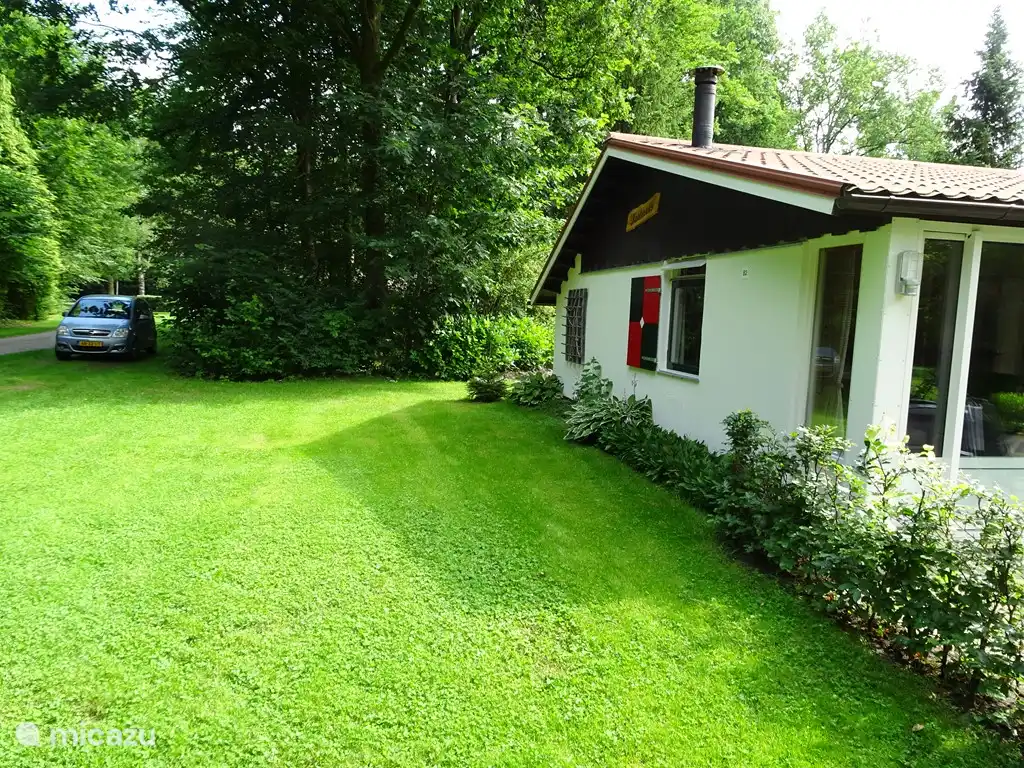 Een bossingel en het gazon scheiden de bungalow van de parkeerplaats.