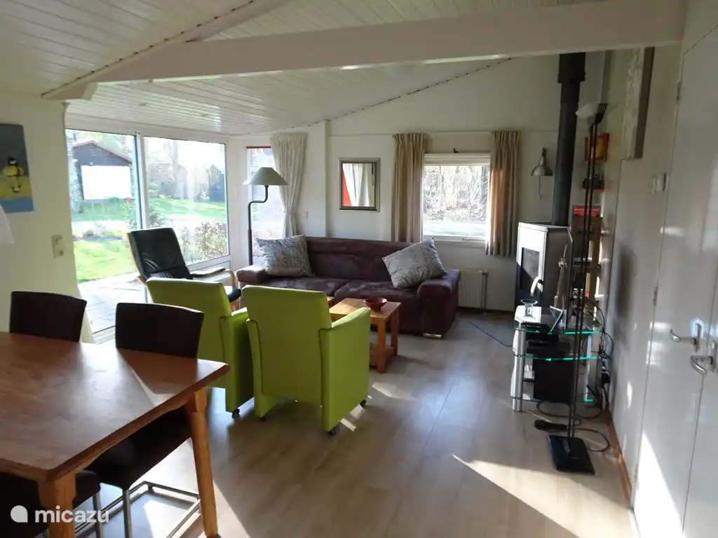 Vanuit de lichte zonnige kamer met schuifpui , heeft men  een fraai ruimtelijk uitzicht op de tuin rondom de vakantievakantiebungalow.