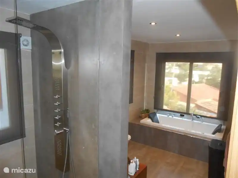 Badezimmer mit Jacuzzi, großer begehbarer (Massage) Dusche, WC und zwei Waschbecken.