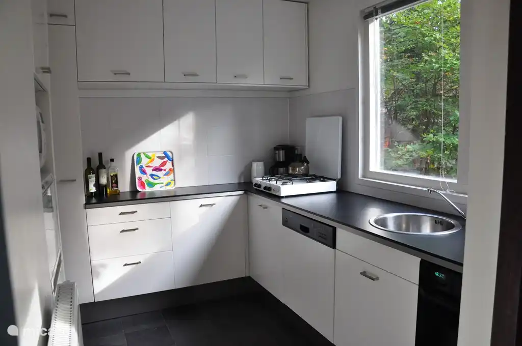 Die Küche mit Fußbodenheizung und Blick auf die Terrasse ist mit einem Geschirrspüler, 4-Flammen-Herd, Kühlschrank, Mikrowelle, Umluftofen und voller Geschirr und Küchenutensilien ausgestattet.