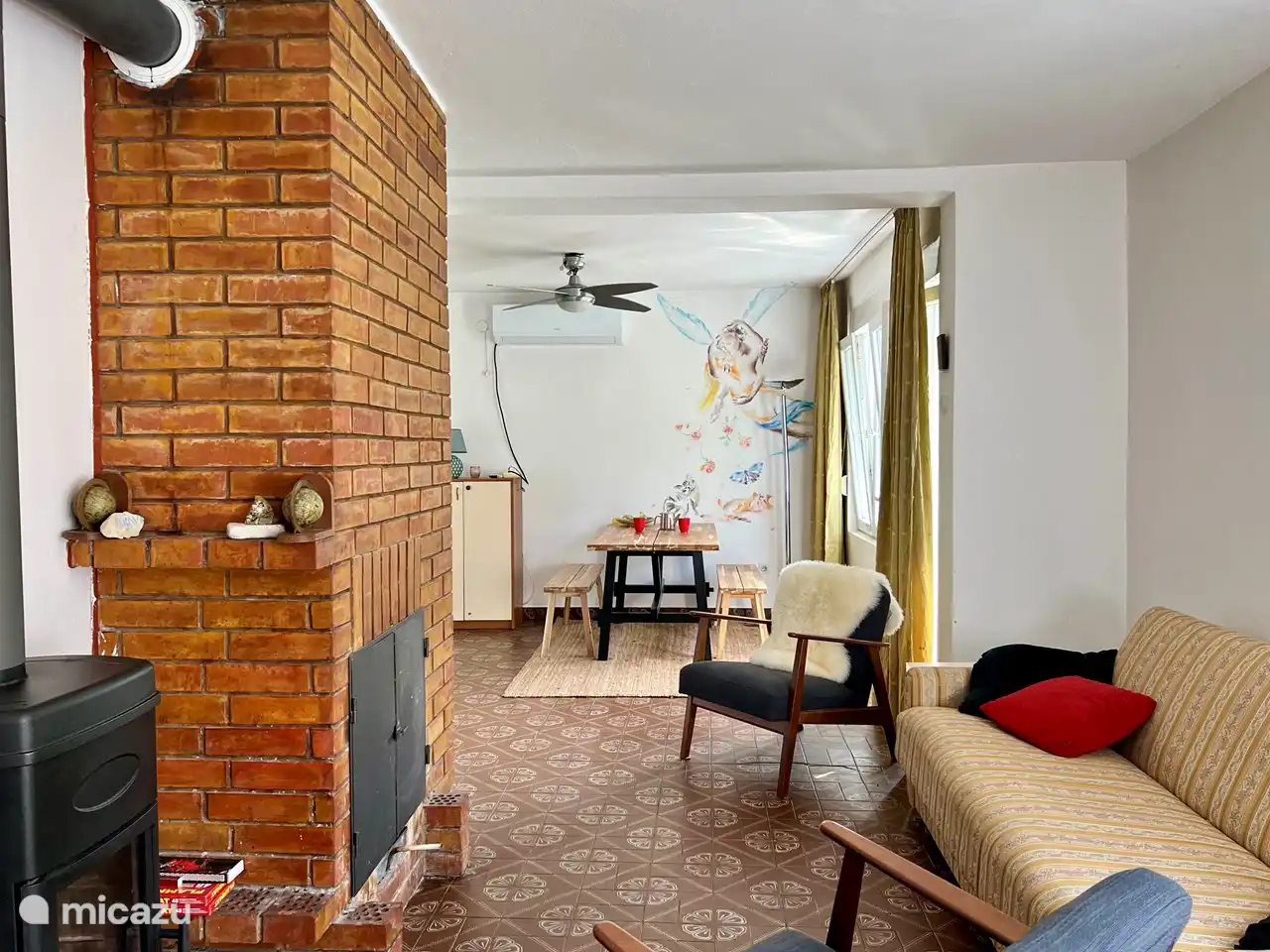 Le salon avec coin repas, système de climatisation, ventilateur d'air et wifi. Cet espace est également équipé d'un divan-lit double, d'un poêle à bois et d'une cheminée. Depuis le salon vous avez accès à 2 balcons, à la cuisine et un escalier à l'étage supérieur,