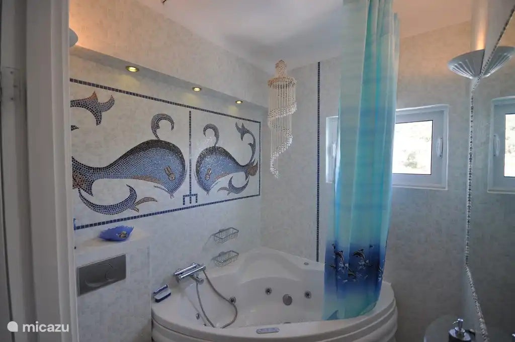 Bad „Artemide“, ein Jacuzzi, Marmorwaschtisch und WC. Das Wandmosaik besteht aus Bildern von zwei Delphinen aus Glasmosaik. Gegenüber einem großen Wandspiegel mit winzigen Schalen ausgekleidet. Eine sehr romantische Suite.