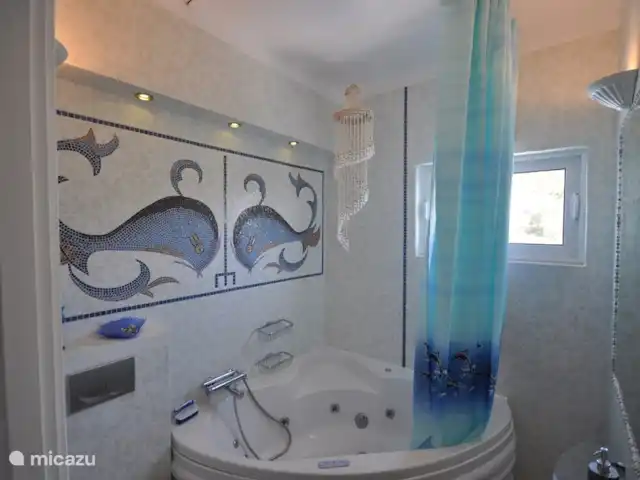Villa individuelle de luxe Livadia | Grèce, Péloponnèse, Kantia - villa Salle de bain Artemide, équipée d'un jacuzzi, lavabo en marbre et toilettes. La mosaïque murale se compose des images de deux dauphins en mosaïque de verre.
En face un mur avec un grand miroir tapissé de petits coquillages. Une salle de bain très romantique.