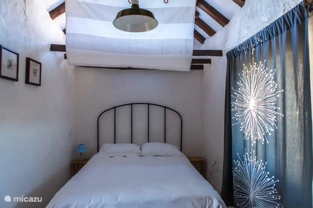 In de slaapkamer staat links het tweepersoonsbed met baldakijn
