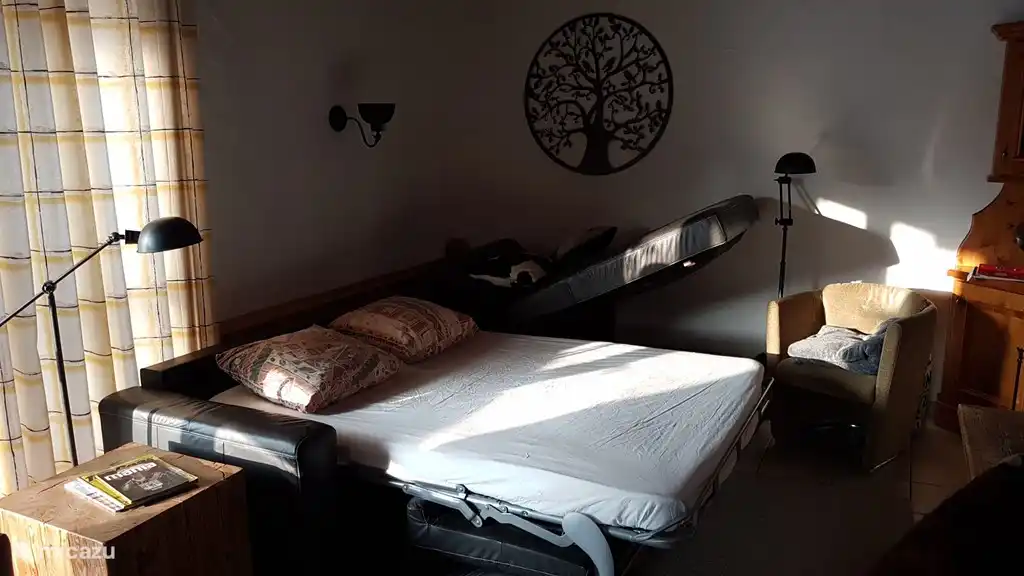 een ruim 2 persoonsbed in de bank van de woonkamer tegenover de openhaard