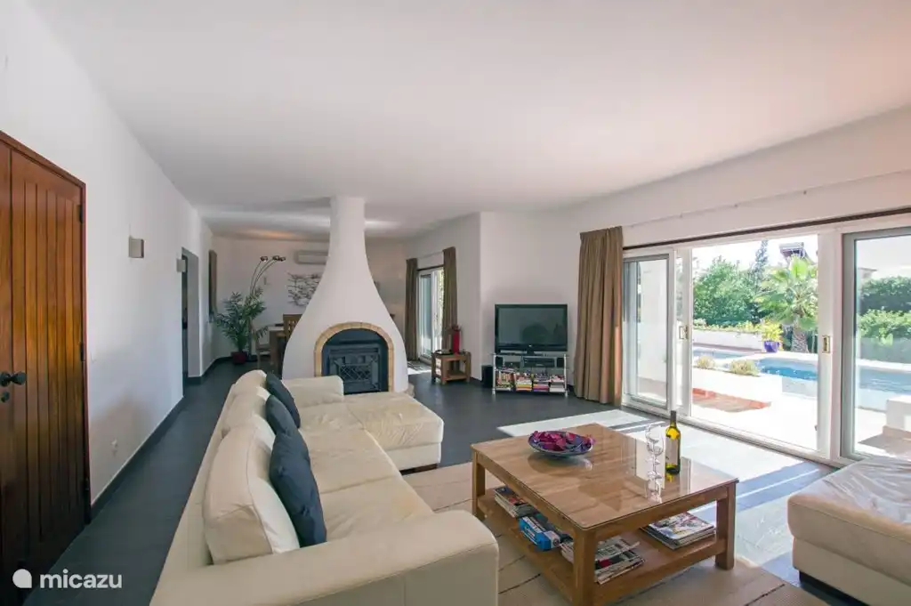 Großzügiger Wohnraum, der von einem großen Kamin mit Holzofen in eine Lounge und einen Essbereich unterteilt ist.