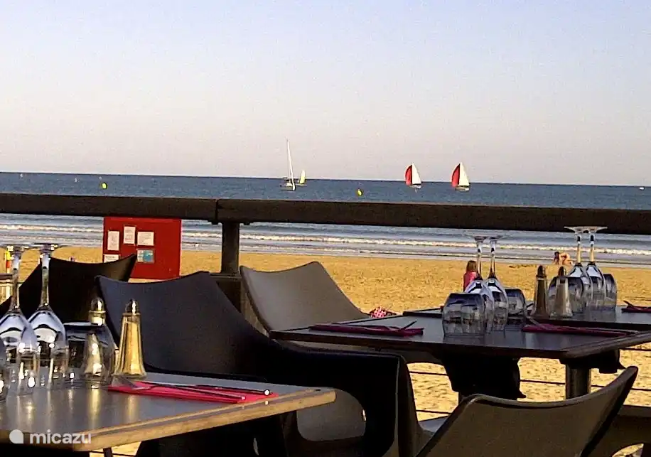 En la playa, buena comida en la terraza mientras los niños juegan cerca en la playa