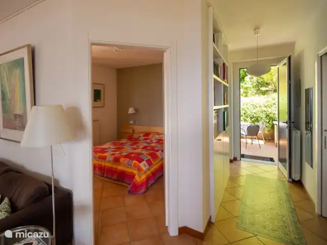 Casa GiaComo | Italie, Lac de Côme, Gravedona - appartement Vue du salon sur la chambre, le couloir avec bibliothèque avec de nombreux livres, magazines, informations touristiques, et la porte d’entrée sur la terrasse arrière