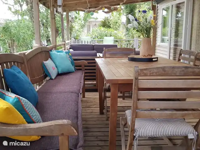 Pampelonne mobilhome aan het strand huren in Frankrijk, Côte d´Azur, Ramatuelle - stacaravan De grote hoekveranda van ruim 55m2 is grotendeels overdekt, daaronder staan een grote eettafel met 2 banken en losse stoelen, een loungeset en twee houten ligbedden met kussens.