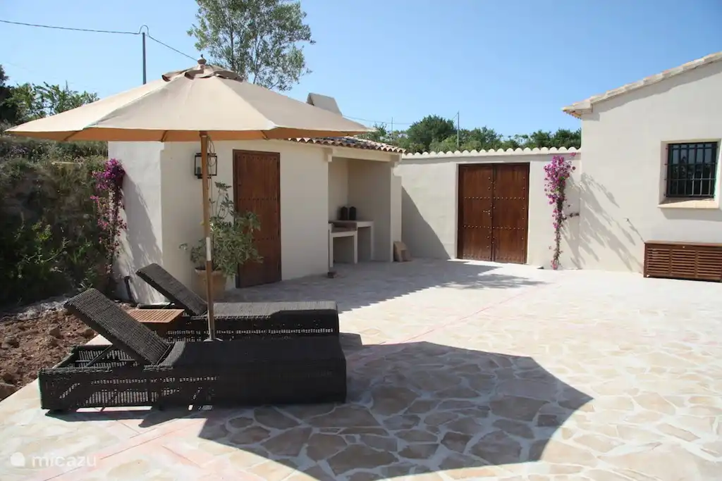 Große Sonnenterrasse mit bequemen Liegestühlen und großen Sonnenschirm.