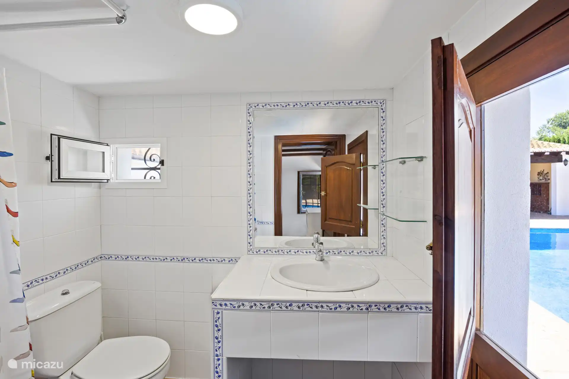 Een nette, verzorgde badkamer met charmante Spaanse tegeltjes en een knipoog naar het zwembad door de deur. Fris jezelf op en spring er zo in!