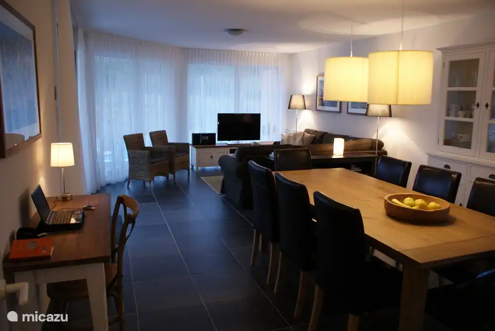 Geräumiges Wohnzimmer mit Sofa, Esstisch für acht Personen und Arbeitstisch.