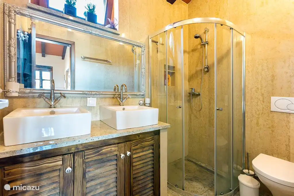 El baño está completamente alicatado con piedra natural y tiene 2 lavabos, un inodoro y una ducha.