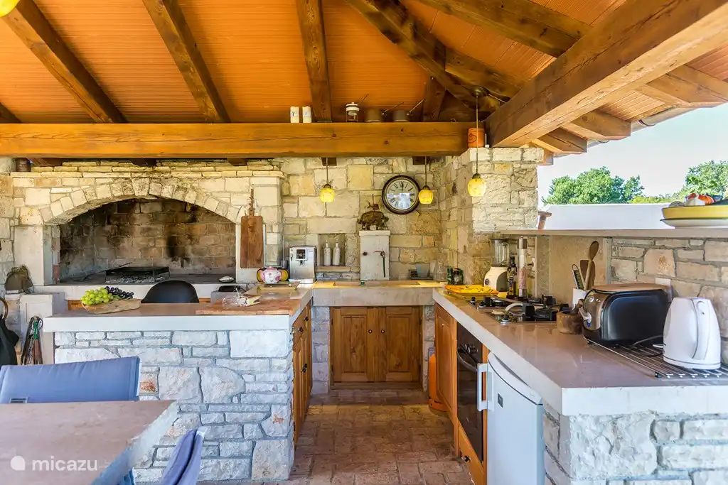 Lujosa cocina al aire libre de estilo tradicional de Istria de 35m2. Dispone de barbacoa de piedra, horno de leña pizzero, gran mesa de comedor de piedra, encimera con fregadero, tostador, lavavajillas, batidora, cocina con wok, tetera, nevera, etc.