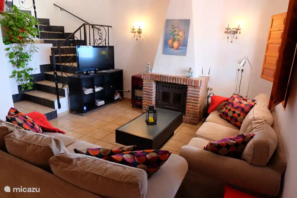 Overzicht zithoek met openhaard  flatscreen TV en de trap naar de bovenverdieping.