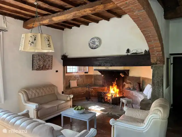 Valpiana | Italie, Toscane, Rufina - villa Le salon a une atmosphère détendue et intemporelle avec une arche en pierre, un plafond en bois et une porte ancienne originale. Il y a une grande cheminée fermière de 1600. Il y a des canapés et des fauteuils, une table avec des chaises, une table basse, une armoire avec des vins, des livres et des jeux de table.