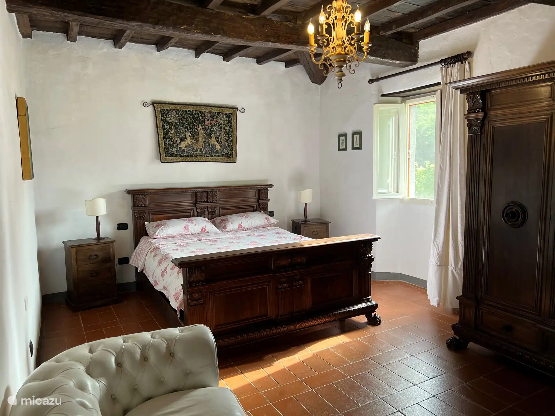 Schlafzimmer mit Doppelbett, geräumigem Kleiderschrank, Zweisitzer-Sofa, Spiegel, Bügelbrett + Bügeleisen, Kleiderbügel aus Holz. Fenster mit schönem Blick auf die Berge, Insektennetz und originalen Markisenpaneelen. 